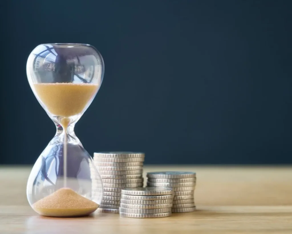 Eine Sanduhr und ein paar Münzen auf einem Schreibtisch für Zeit sparen mit Distler Immobilien